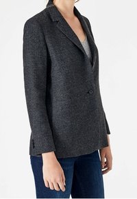Tmavě šedý herringbone blazer s jedním knoflíkem, klopami a mírným střihem. Dlouhé rukávy s knoflíkovými detaily.