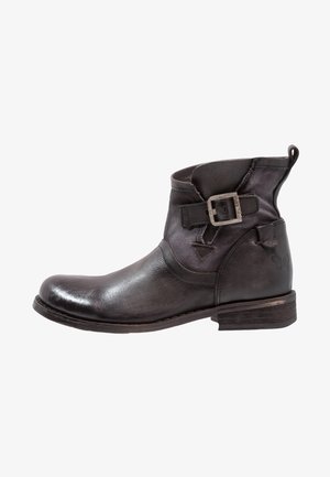 Bottine en cuir noir avec petit talon, bride à boucle latérale et languette à l'arrière, présentée de profil sur un fond blanc.