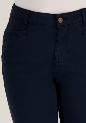 Vooraanzicht van marineblauwe broek met knoop- en ritssluiting, zichtbare voorkanten zakken, gedragen met een witte top.