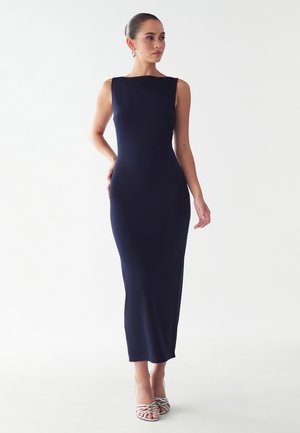 Navy blue fitted sleeveless dress, knee-length, with a smooth texture. Worn with strappy silver high-heeled sandals. Plain background.