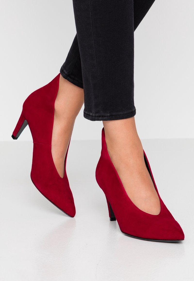 Zapatos de tacón alto de ante rojo con puntera puntiaguda y laterales recortados, con un delgado tacón de aguja y suela negra.