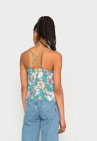 Camisola com estampa floral em verde-água com finas alças cruzadas nas costas. O tecido texturizado apresenta grandes padrões de flores coloridas.
