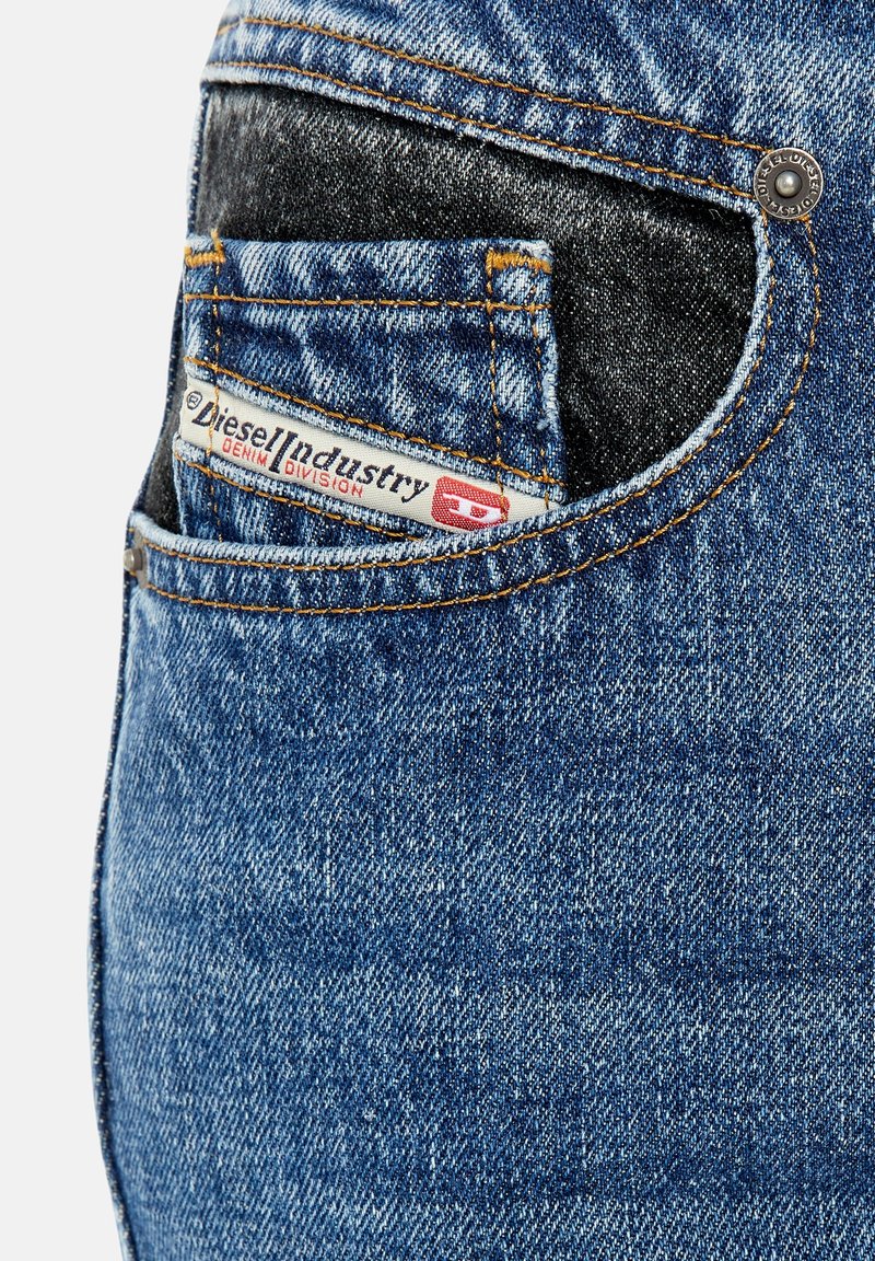 Jeans in denim blu con una tasca posteriore scura a contrasto, caratterizzati da cuciture gialle e un'etichetta "Diesel Industry" ben visibile nella tasca.