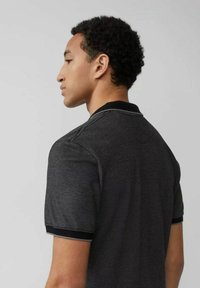 Schwarzes Poloshirt aus strukturiertem Stoff, mit kontrastierendem Kragen und Bündchen. Zeigt eine taillierte Silhouette und minimalistische Designelemente.