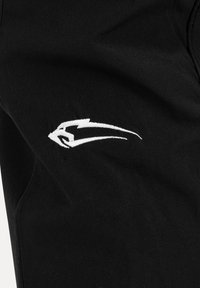 Logo de tête d'animal stylisée blanche, ressemblant à un faucon ou un aigle, brodé sur tissu noir, peut-être un vêtement ou un accessoire.