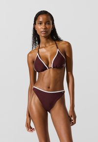 Pruun bikiinikomplekt, millel on kolmnurkne tops valgete lõhestatud äärega ja sobivad kõrge vöökohaga aluspüksid. Sile tekstuur ja minimaalne disain.
