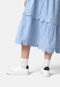 Nohy v bílých krajkových ponožkách, bílých teniskách s černými patními pásky a modro-bíle károvaných šatech s krajkovými okraji.