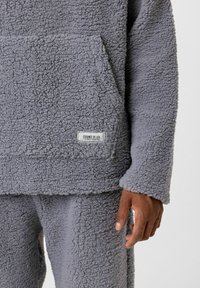 Gezellige grijze fleece hoodie met een gestructureerde afwerking, voorzien van een voorzak en een label met de tekst "ESSENCE OF LIFE." Zacht, warm materiaal.