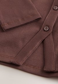 Cardigan côtelé marron avec boutons, finitions soignées sur les bords, texture douce, mettant en avant les lignes verticales du tissu.
