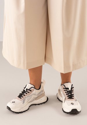 Zapatos deportivos blancos y negros con materiales de malla y sintéticos, que presentan un diseño texturizado, cordones negros y una suela gruesa.