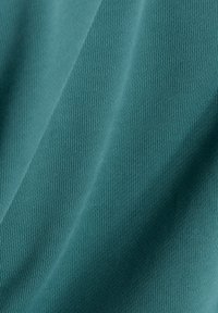 Tela de algodón color verde azulado con una textura acanalada, presenta líneas verticales y una superficie suave y lisa. Sombras y luces crean profundidad.