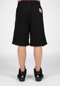Black woven shorts with an elastic waistband, featuring a back pocket and a small label. Paired with black high-top sneakers.
