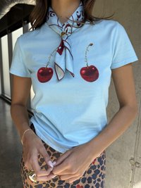 Světle modrá košile s krátkým rukávem s červenými grafickými detaily třešní. Doplněná vzorovaným šátkem uvázaným kolem krku.