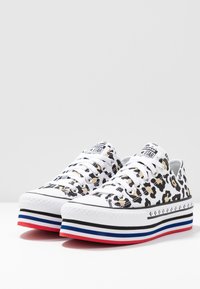 Sneaker basse con stampa leopardata bianca, nera e beige, lacci bianchi e suole spesse a piattaforma striate di rosso, bianco, blu e nero.