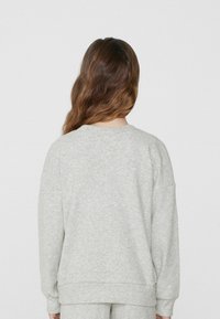 Šedá mikina s měkkou texturou, uvolněným střihem, kleslými rameny a ribbenovými manžetami. Zadní strana má jednoduchý design bez ozdob.