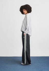 Pilkas, struktūrinis džemperis su baltais dryžiais; juodos, plačios kelnės su trimis baltais šoninėmis juostelėmis; pilki sportbačiai.