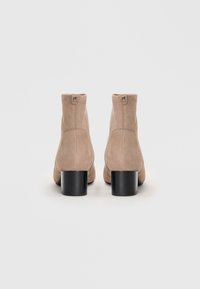 Beige suède enkellaarsjes met een ronde neus, hoge schacht en een stevige zwarte hak. Heeft een minimalistisch ontwerp met een discreet logo.