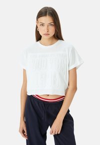 Witte, cropped T-shirt met reliëftekst "LOS ANGELES TEAM GOOD VIBE 1998." Korte mouwen en ronde halslijn; van zacht katoen.