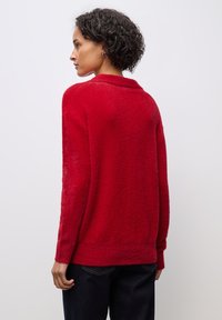 Roter, flauschiger Pullover mit lässiger Passform, langen Ärmeln und geripptem Saum. Die Textur scheint weich und warm zu sein, geeignet für legere Kleidung.