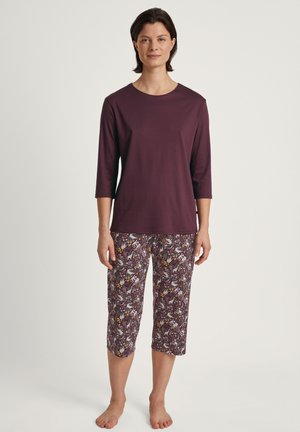Bordeaux driekwart mouwtop gecombineerd met een cropped broek met een kleurrijk bloem- en abstract patroon op een lichte achtergrond.