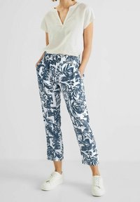 Bílé tričko s krátkým rukávem v kombinaci s tmavě modrými zkrácenými kalhotami s listovým vzorem. Kalhoty mají elastický pas a boční kapsy. Bílé tenisky.