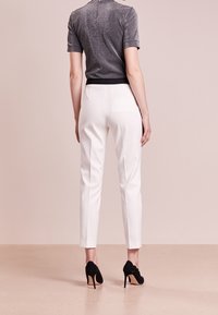 Pantalons blancs sur mesure avec une coupe slim, dotés d'une poche arrière et associés à un haut gris ajusté et scintillant ainsi qu'à des chaussures à talons hauts noires.