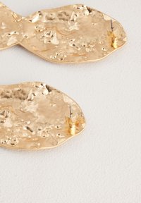 Gold-toned metal earrings with a textured, irregular shape and a stud backing for secure wear. Rich, reflective surface detailing.