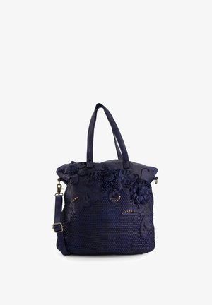 Navy blue handbag with textured floral accents, woven base, dual shoulder straps, and a removable crossbody strap. Features gold studs.