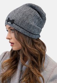 Berretto in maglia grigio con motivo testurizzato, accentato da un fiocco nero e cuciture a contrasto nere lungo l'orlo. Design leggero e morbido.