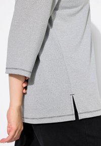 Top a righe grigie realizzato in tessuto leggero, con orlo arrotondato e spacchi laterali, e maniche a tre quarti.