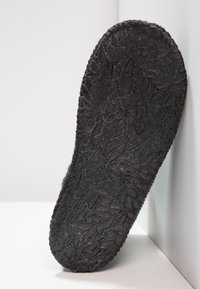 Zwarte, gestructureerde zool met een bladmotief, gemaakt van rubberachtig materiaal. Gladde rand met licht verhoogde ribbels langs de omtrek.