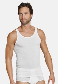 Hvid ribbet tanktop med en klassisk pasform, der har en rund halsudskæring og brede skulderstropper. Bæres med matchende hvide briefs.