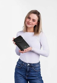 Černá kožená peněženka s zakřiveným klopou, zipovým uzavřením a detailem loga. Držena v ruce, s hladkým povrchem a kompaktním designem.