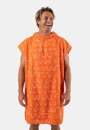 Man lacht, draagt een oranje mouwloze hooded tuniek bedekt met verschillende witte abstracte lijnen tekeningen van borsten, staand tegen een witte achtergrond.