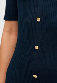 Μπλε ναυτικό ριμπ πλεκτό τοπ με κοντά μανίκια, που διαθέτει πέντε χρυσά κουμπιά ως διακοσμητικά στην μπροστινή πλευρά για μια υφασμάτινη αίσθηση.