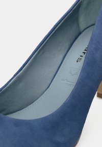 Μπλε σουέτ ψηλοτάκουνα παπούτσια με λεία εσωτερική επένδυση και μεσαίου ύψους ανοιχτόχρωμο ξύλινο τακούνι. Η κοντινή λήψη τονίζει την υφή και το σχήμα.