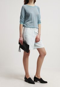 Ljusblå tröja i texturerad stickning med trekvartsärmar, kombinerad med vita skräddarsydda shorts, svarta platta skor och en svart clutch.