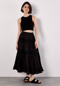 Top corto nero abbinato a una gonna maxi nera a strati con dettagli in pizzo. L'outfit è completato da sandali neri in stile slide.