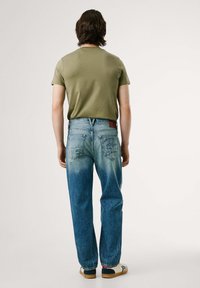 Una camiseta verde de manga corta combinada con unos vaqueros azules desgastados que presentan un degradado del color claro al oscuro y dos bolsillos traseros. Calzado casual completa el look.