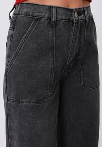 Jean en denim noir taille haute avec une finition texturée, dotés de poches angulaires, de coutures visibles et d'une fermeture à bouton.