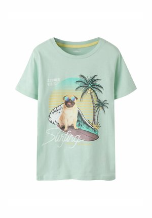 Camiseta verde claro con un carlino con gafas de sol sentado en una tabla de surf, palmeras, puesta de sol y el texto "Vibras de Verano" y "Surf".