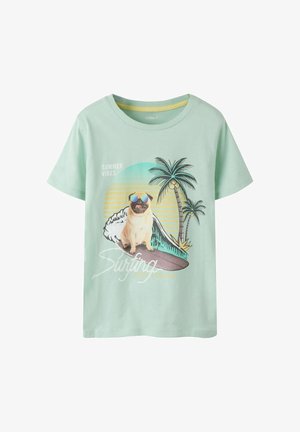 Ανοιχτό πράσινο T-shirt με έναν παγκ που φοράει γυαλιά ηλίου και κάθεται σε σανίδα του σερφ, φοίνικες, ηλιοβασίλεμα και κείμενο "Καλοκαιρινές Δονήσεις" και "Σέρφινγκ".