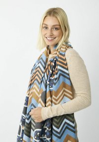 Écharpe à motif chevron colorée en bleu, marron et vert, fabriquée en tissu doux et texturé, drapée sur les épaules.