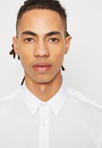 Camisa branca de botões com colarinho clássico e textura de tecido suave. Apresenta um fecho frontal com botões e um design ajustado.