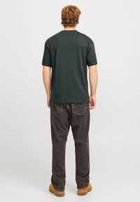 Camiseta de algodón verde oscuro con mangas cortas y cuello redondo, combinada con pantalones sueltos marrón oscuro y calzado marrón. Diseño sencillo sin patrones.