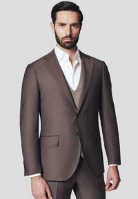 Brąsuowy garnitur o dopasowanym kroju, z klapami w kształcie litery V oraz dwiema przednimi kieszeniami. Nosi się go na kremowej koszuli i fakturowanej kamizelce.