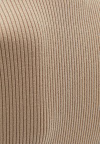 Beiger, gerippter Stoff mit einer weichen Textur, der durchgehend vertikale Streifen aufweist. Das Material wirkt glatt und samtig.