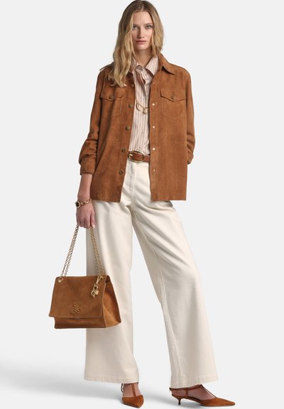 Braune Wildleder-Hemdenjacke mit zwei Brusttaschen, gestreiftes Hemd, cremefarbene, weit geschnittene Hose und eine beige Handtasche mit goldenen Akzenten.