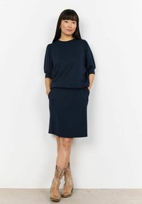 Abito blu navy con vestibilità comoda, maniche corte e tasche. Presenta una consistenza liscia e una lunghezza che termina appena sopra il ginocchio.