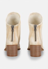 Bottines en cuir crème avec un bout rond, des fermetures éclair sur les côtés et des talons en bois empilés, présentant une texture lisse et un design structuré.